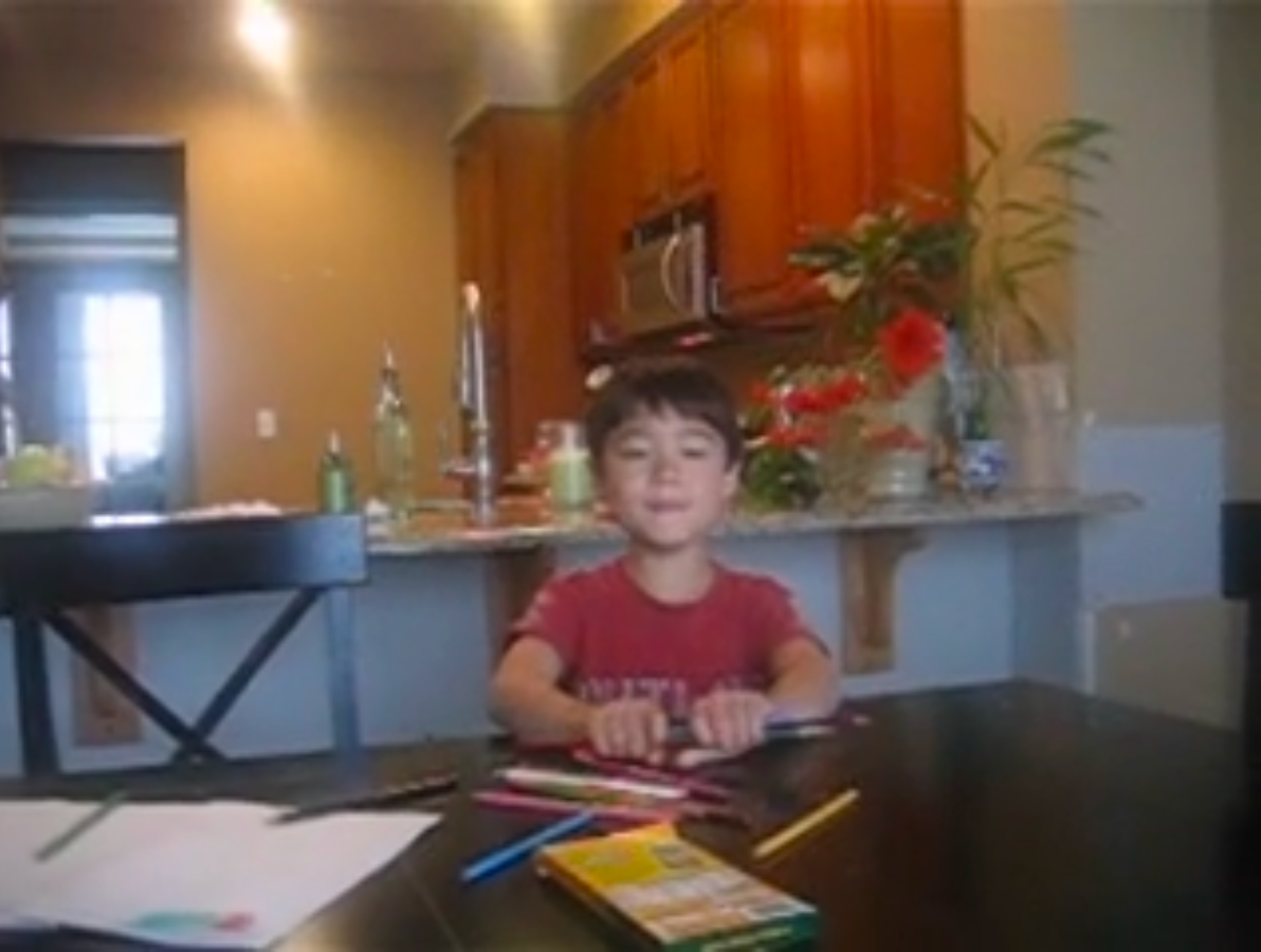 Young Zach Hirata holding colored pencils while being filmed creating a homemade cookbook